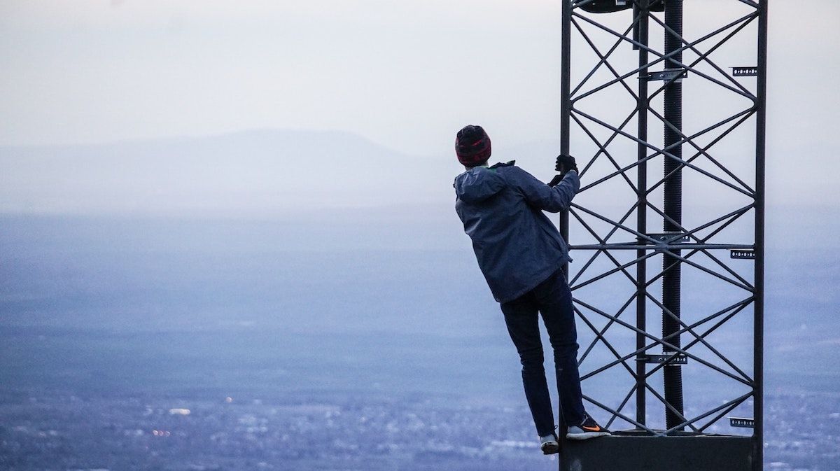 Person hanging on to a cell tower and gazing at a landscape